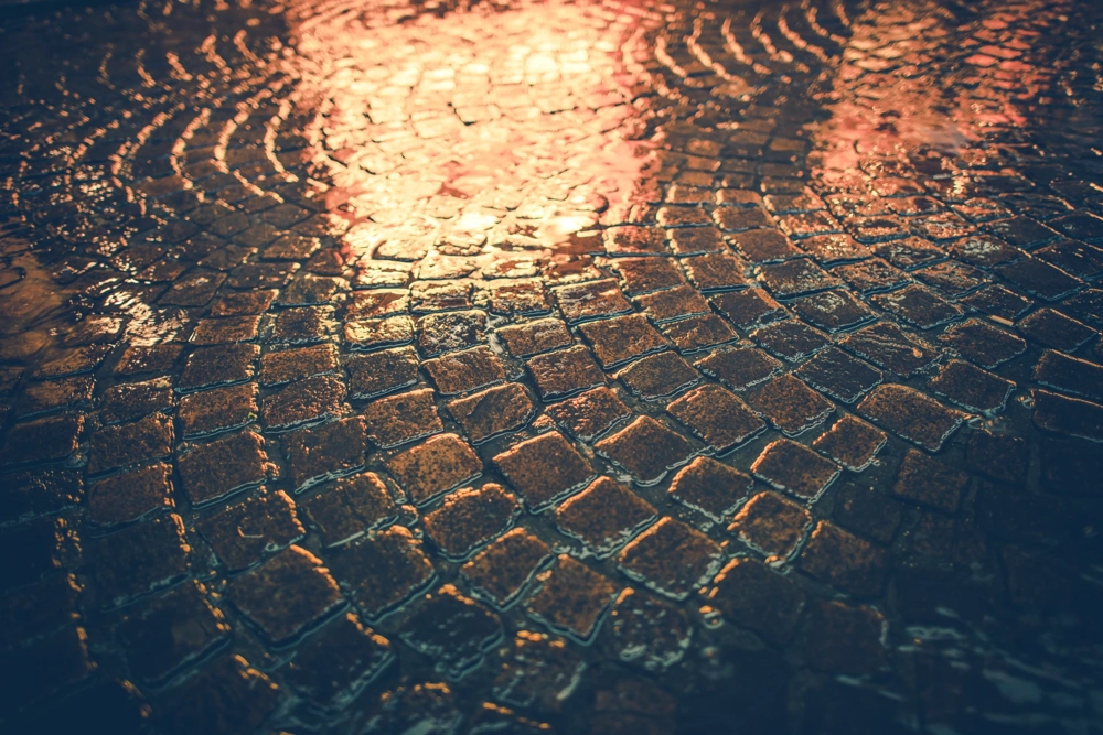 Mycie kostki brukowej – zbliżenie czystej, mokrej kostki brukowej z lśniącą wodą i refleksami światła